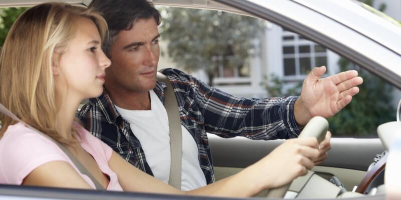 Man and girl in car with man gesturing ahead