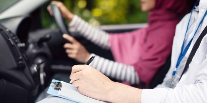 Examiner marking test sheet with girl driving