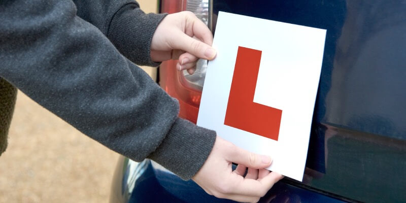 Two hands placing a learner sign onto rear of the car
